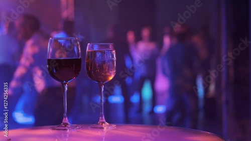 Two glasses of red and white wine on table with dancing crowd in background. Captures nightlife, celebration moments within vibrant, atmospheric club setting.