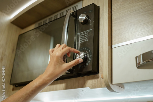 Obraz na plátně Woman's hand adjusting time with circle button to heat food from microwave in modern kitchen, interior style of the campervan or motorhome