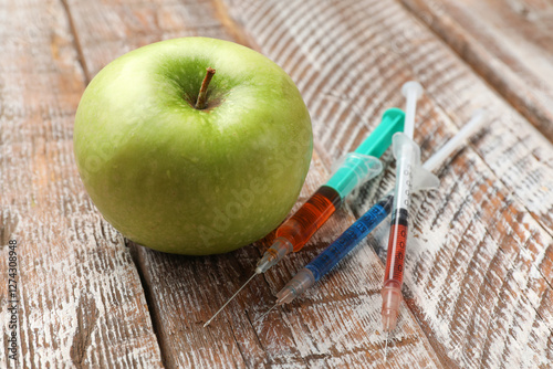 GMO concept. Green apple and syringes on rustic wooden table, closeup