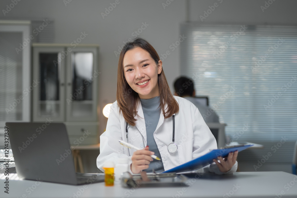 Smiling asian female doctor working with documents and laptop at hospital office
