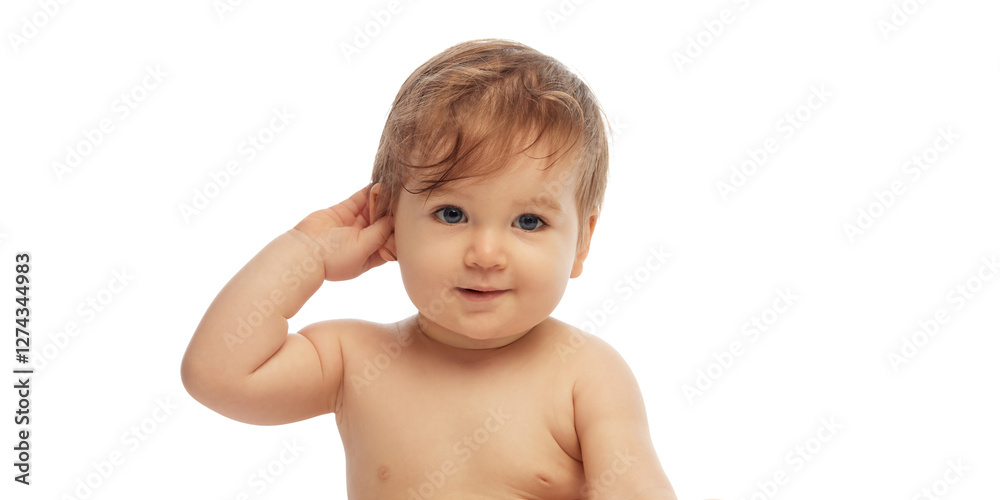 Portrait of little, adorable baby touching ear with hand while smiling and gazing forward against white background. Concept of childhood, discovery, sensory development, emotions. Portrait of little, adorable baby touching ear with hand while smiling and gazing forward against white background. Concept of childhood, discovery, sensory development, emotions.