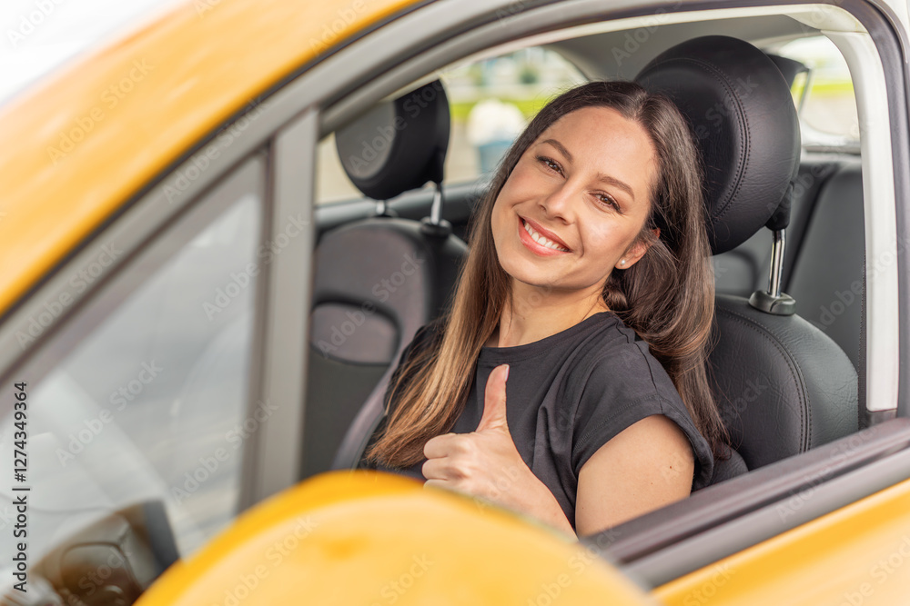 A young woman with long brown hair and a bright smile sits in the driver's seat of a yellow car, giving a thumbs-up gesture through the open window with a confident and positive expression.