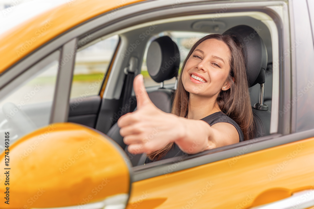 A young woman with long brown hair and a bright smile sits in the driver's seat of a yellow car, giving a thumbs-up gesture through the open window with a confident and positive expression.