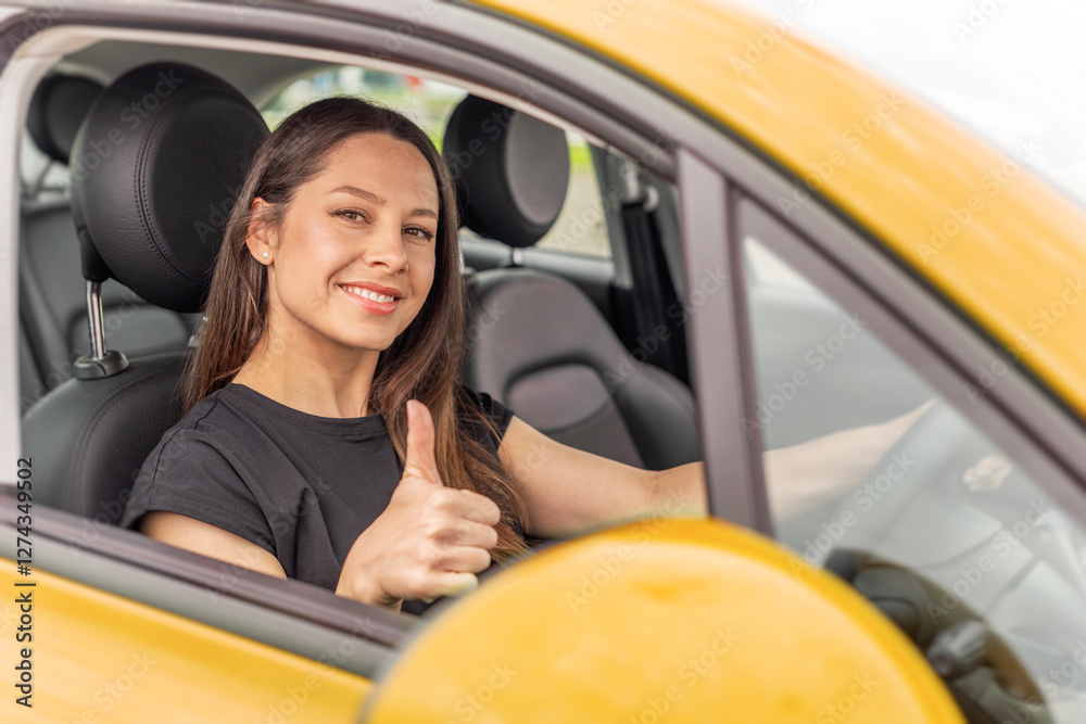 A young woman with long brown hair and a bright smile sits in the driver's seat of a yellow car, giving a thumbs-up gesture through the open window with a confident and positive expression.