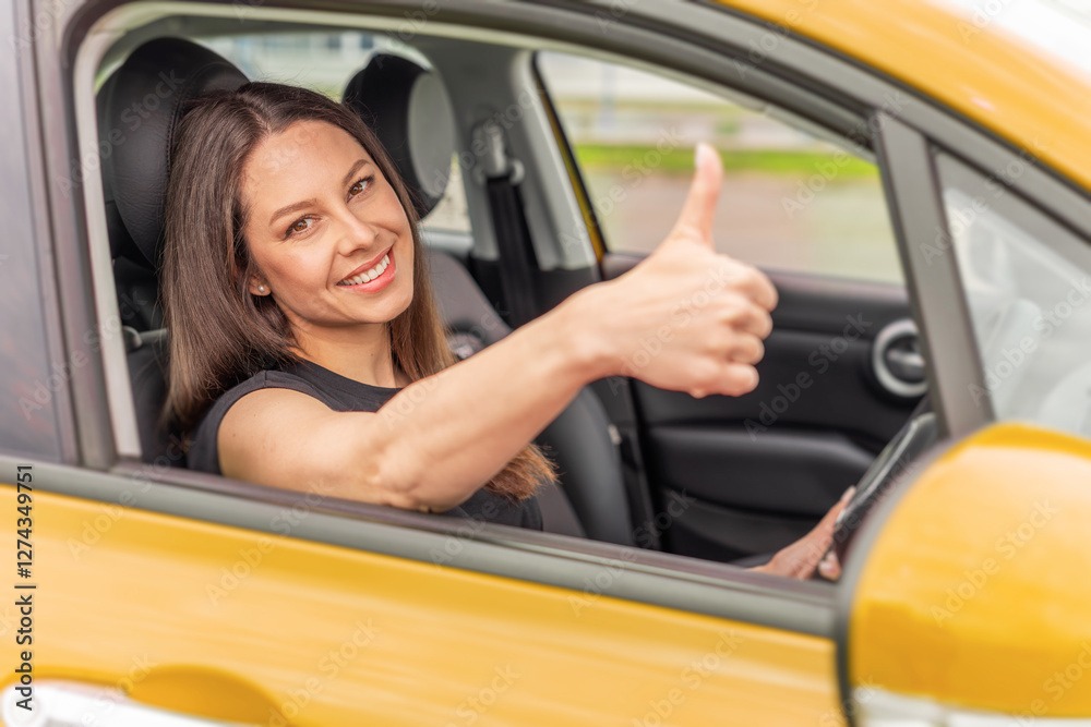 A young woman with long brown hair and a bright smile sits in the driver's seat of a yellow car, giving a thumbs-up gesture through the open window with a confident and positive expression.