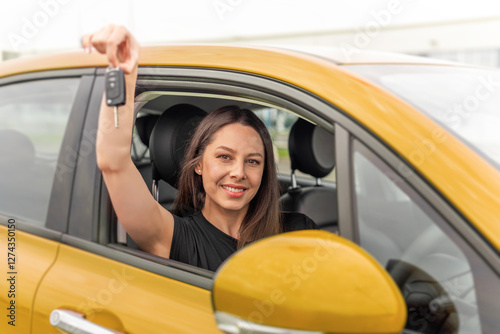 Obraz na płótnie A young woman with long brown hair and a bright smile sits in the drivers seat of a yellow car, happily holding up a set of car keys through the open window. w salonie