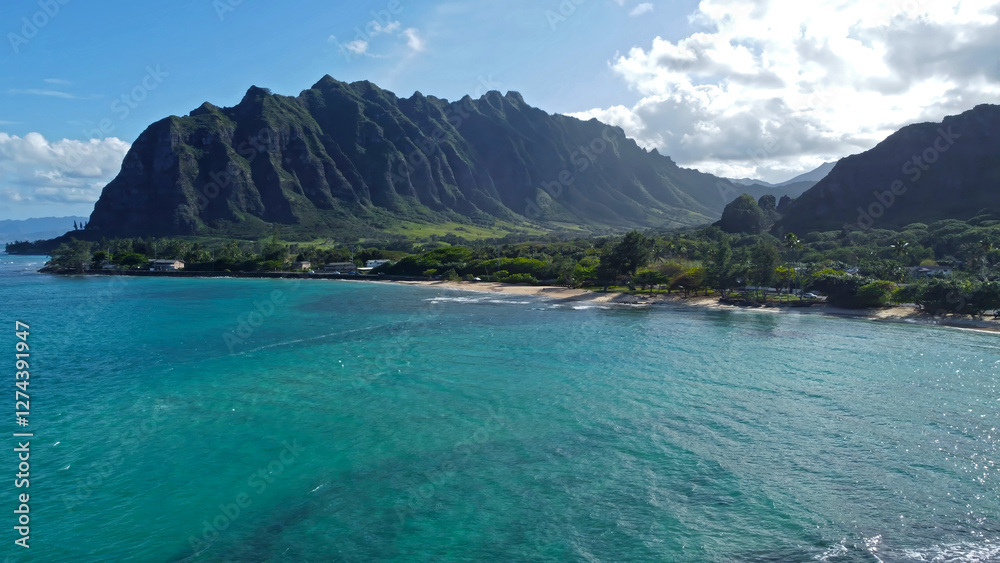 Fototapeta premium Kualoa Mountains and turquoise ocean, scenic Hawaiian coastline with lush greenery and sandy beach.