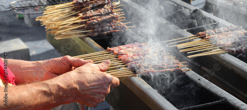 Large hands of the shepherd cooking ARROSTICINI, a typical dish of Central Italy, on the grill