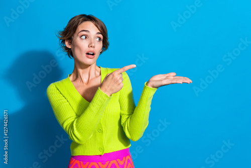 Photo of pretty impressed girl look direct finger arm hold empty space information isolated on blue color background