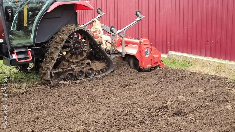A mini crawler tractor with a cutter works on an agricultural field, milling the soil. A mini crawler tractor with a cutter works on an agricultural field, milling the soil.