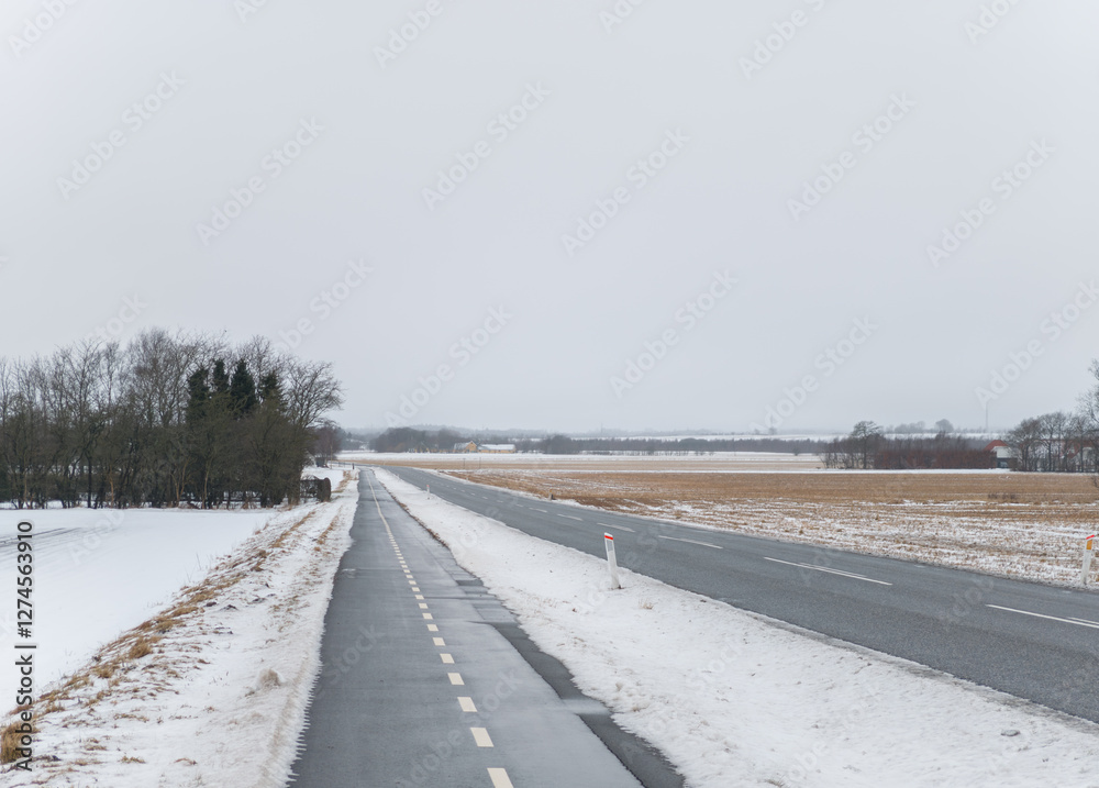 Winter landscape somewhere in Aalborg kommune, Nordjylland, Denmark. Car road along with a bicycle path and wheat field covered in snow.