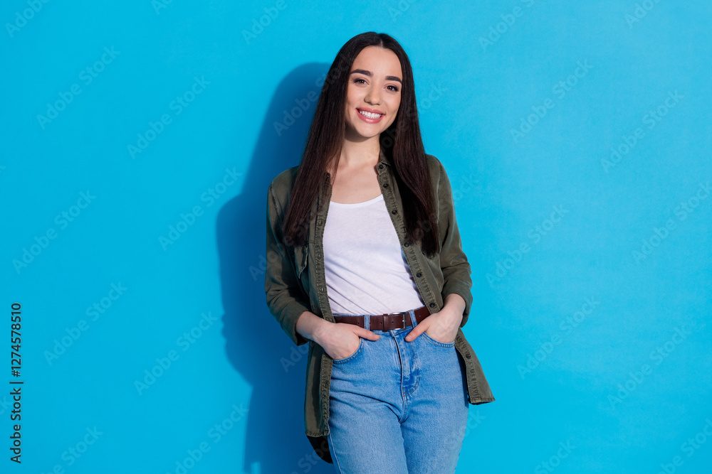 Smiling young woman stands against blue backdrop exuding confidence and style in casual fashion Smiling young woman stands against blue backdrop exuding confidence and style in casual fashion