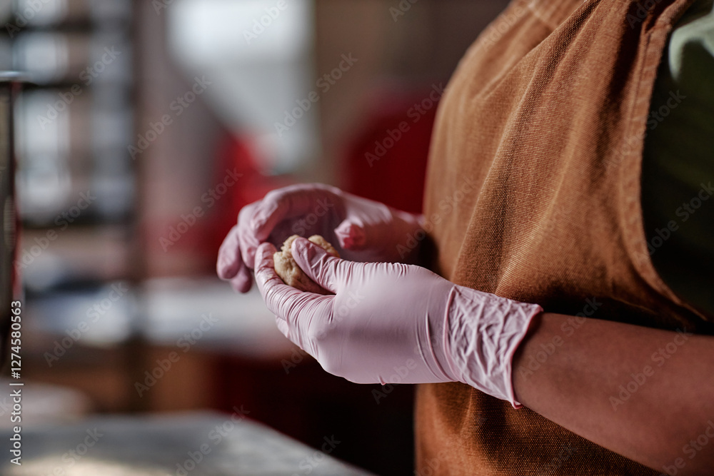 Obraz premium Cropped shot of unrecognizable Black female baker working in nitrile disposable gloves forming piece of raw dough making round wheat buns in bakehouse kitchen, copy space