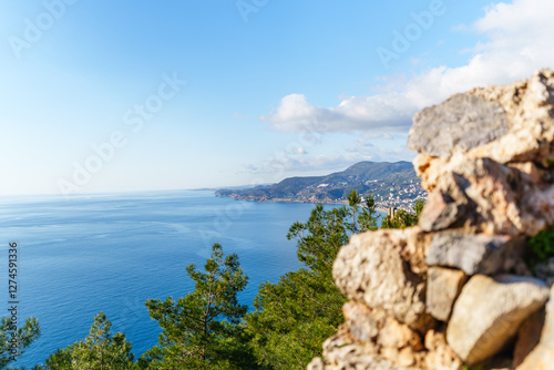 Fototapeta Naklejka Na Ścianę i Meble -  A picturesque coastal scene of Alanya Kleopetra beach and castle with a serene blue sea, lush trees, and distant mountains..