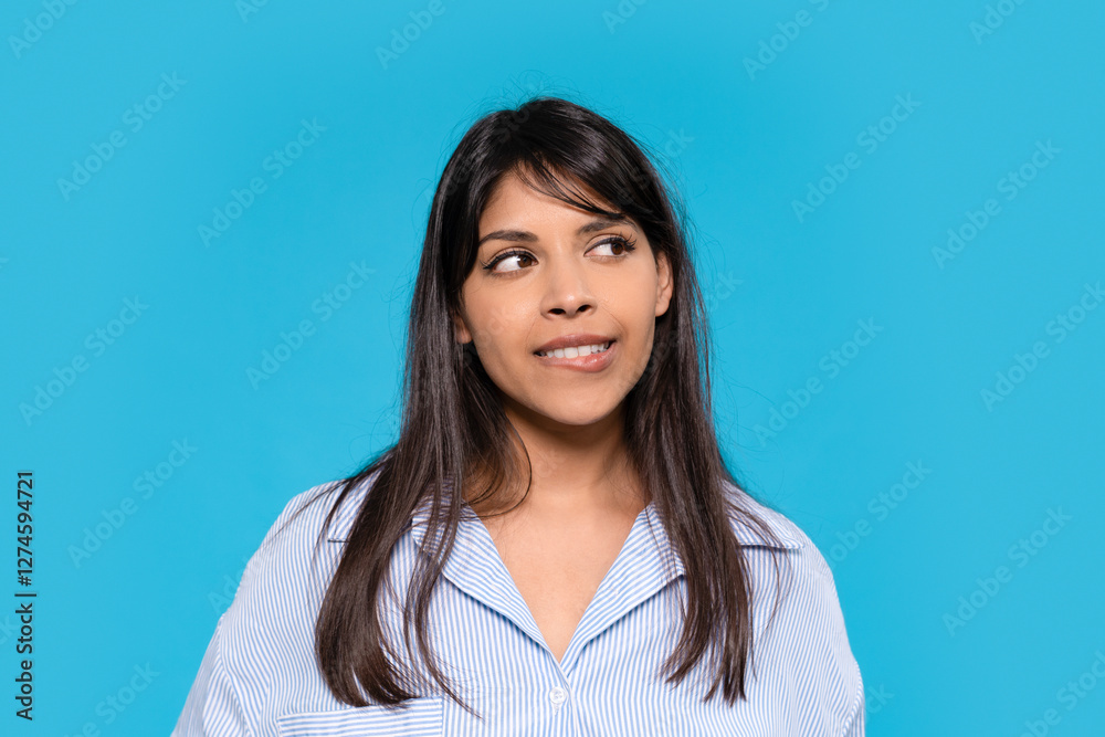 Expressive young woman smiling playfully against solid blue background in casual attire Expressive young woman smiling playfully against solid blue background in casual attire