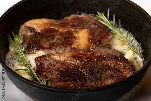cooking beef steak in a frying pan in butter with garlic and rosemary