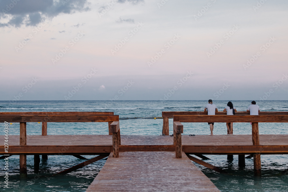 People enjoying a serene sunset on a wooden pier in Tulum People enjoying a serene sunset on a wooden pier in Tulum