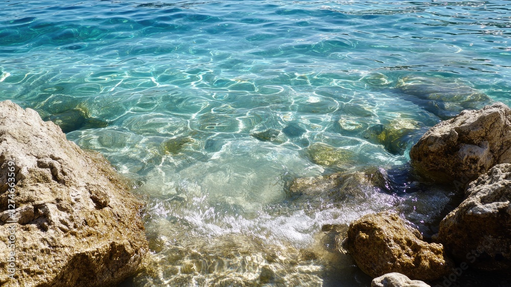 Clear turquoise seawater with rocky shore, reflecting sunlight Clear turquoise seawater with rocky shore, reflecting sunlight