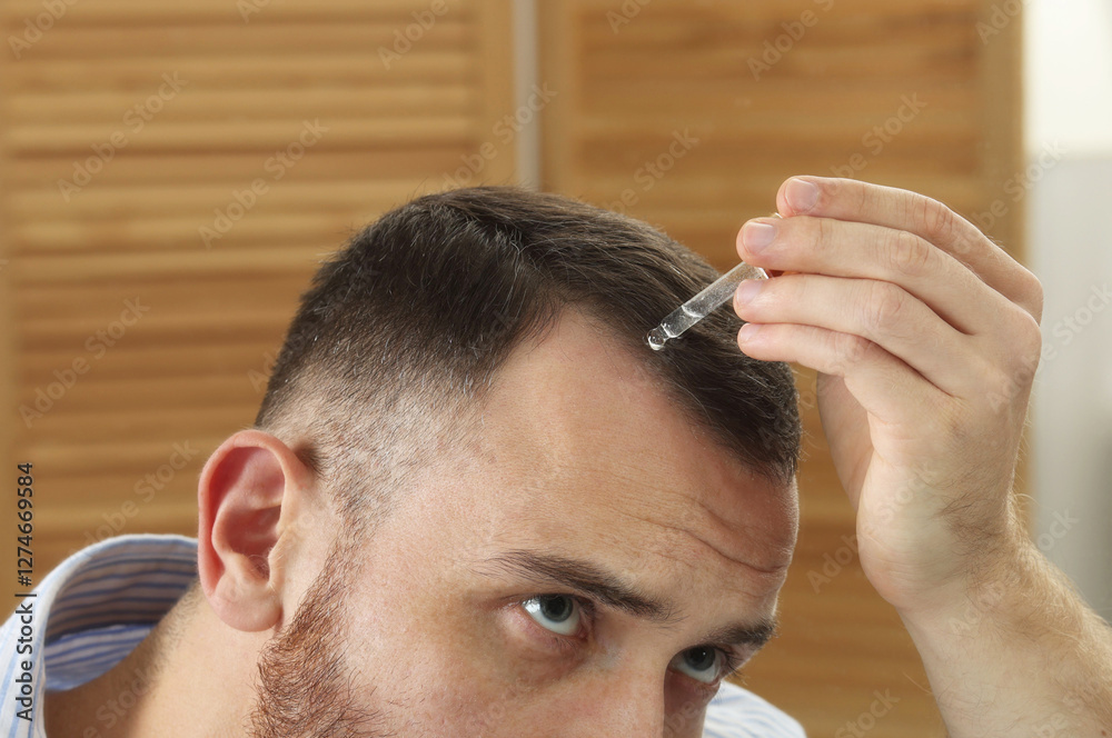Obraz premium Baldness treatment. Man applying serum onto hair at home, closeup