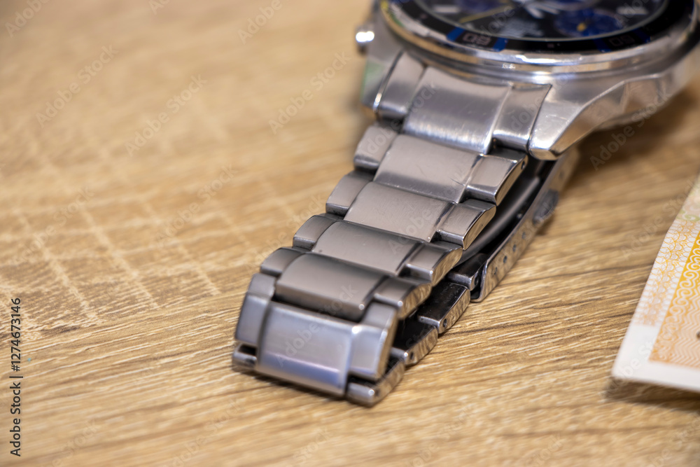 Close-up view of a stylish silver watch, highlighting its intricate design and sleek bracelet, resting on a wooden surface. Ideal for fashion and lifestyle themes. Close-up view of a stylish silver watch, highlighting its intricate design and sleek bracelet, resting on a wooden surface. Ideal for fashion and lifestyle themes.