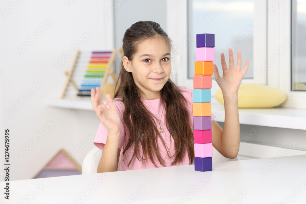 Happy girl with tower of colorful cubes at table indoors Happy girl with tower of colorful cubes at table indoors