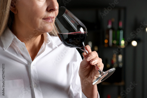 Professional sommelier tasting red wine indoors, closeup photo