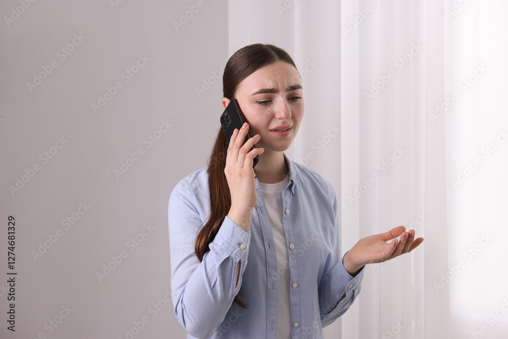 Stressed woman calling hotline for mental health help near window at home Stressed woman calling hotline for mental health help near window at home