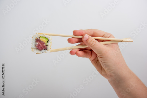 Hand Holding Sushi California Roll with Chopsticks on White Background