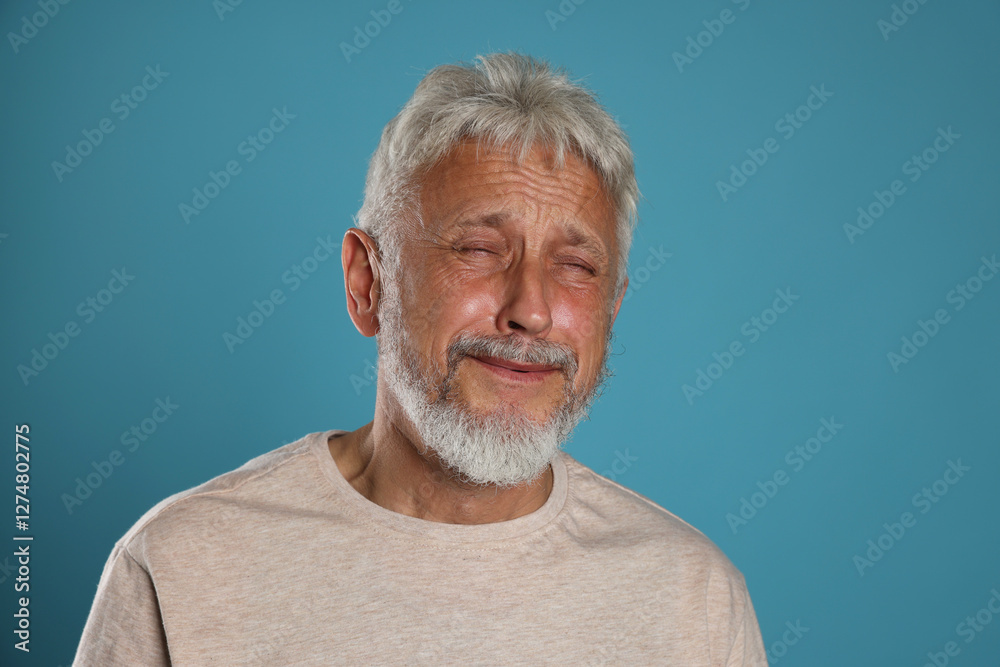 Sad senior man crying on light blue background Sad senior man crying on light blue background