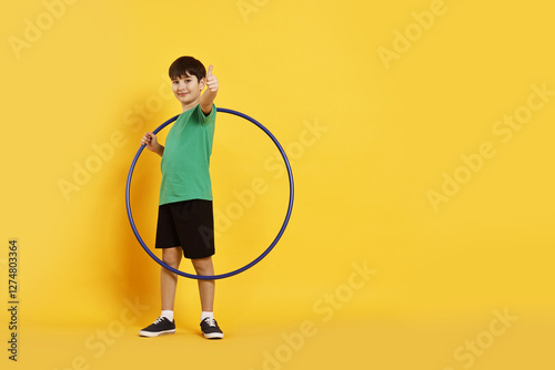 Boy with hula hoop showing thumbs up on yellow background, space for text photo