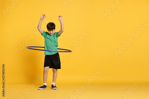 Boy exercising with hula hoop on yellow background, space for text photo