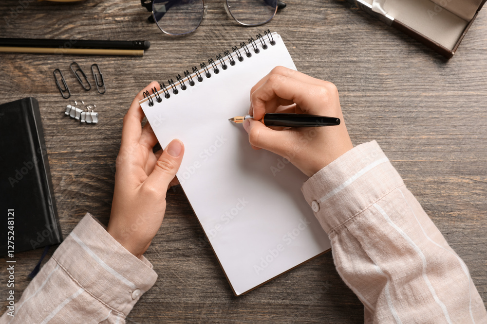 Female hands with blank notebook, fountain pen, eyeglasses and stationery on wooden table, closeup Female hands with blank notebook, fountain pen, eyeglasses and stationery on wooden table, closeup