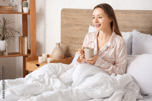 Young woman in bed with cup...
