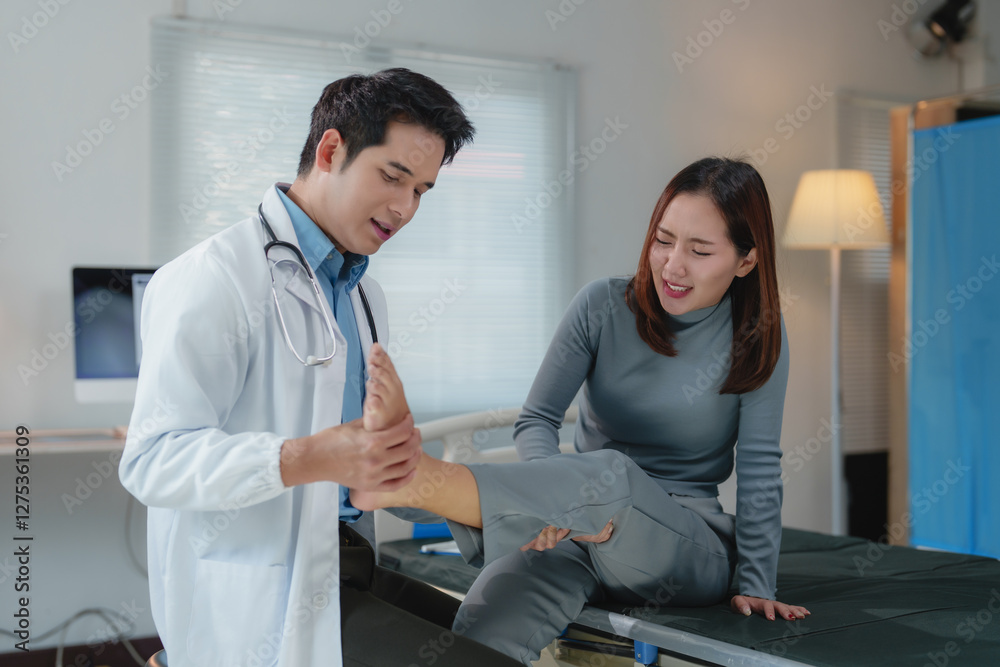 Fototapeta premium Asian male doctor examining injured ankle of young female patient who is experiencing pain while sitting on examination bed in hospital room