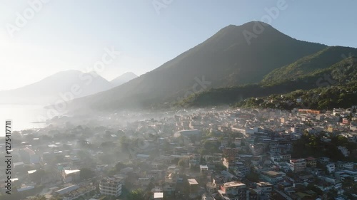 San Pedro La Laguna village and the serene Lake Atitlan captured at sunrise in lush tropical scenery, atmospheric mist covers buildings, aerial overview photo