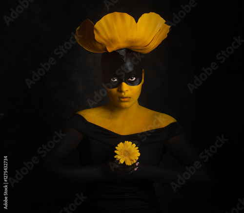 Obraz na płótnie A woman dressed vibrantly in black and yellow holding a yellow flower w salonie