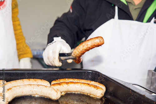 Adult handling grilled sausages with tongs at outdoor event