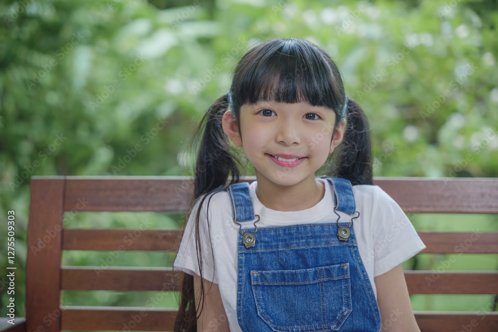Asian young attractive girl seated on wooden bench in the garden scenic outdoor setting, Kid sitting on the bench in nature park Asian young attractive girl seated on wooden bench in the garden scenic outdoor setting, Kid sitting on the bench in nature park
