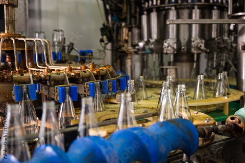 A conveyor in a modern distillery features empty glass bottles for alcoholic beverage production and bottling. The automated clean factory assures efficient manufacturing. photo