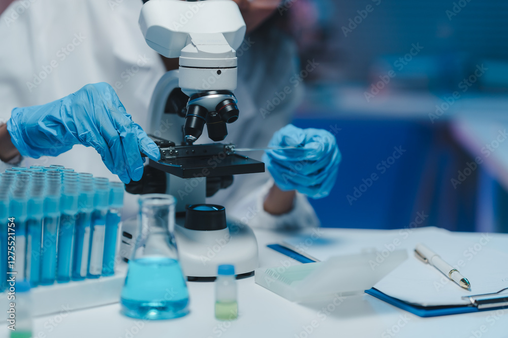 Gloved hands positioning a microscope slide on a modern microscope stage, surrounded by lab equipment like test tubes and beakers, conducting scientific research Gloved hands positioning a microscope slide on a modern microscope stage, surrounded by lab equipment like test tubes and beakers, conducting scientific research