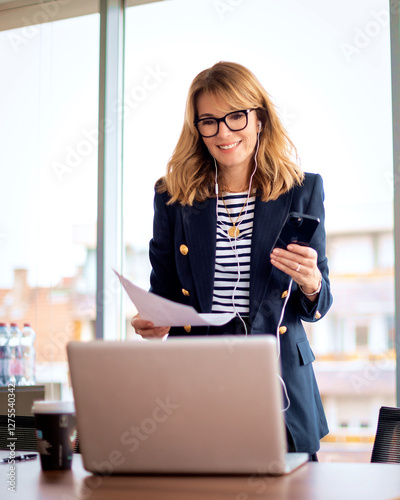 Blond haired woman using smartphone and laptop in a modern office photo