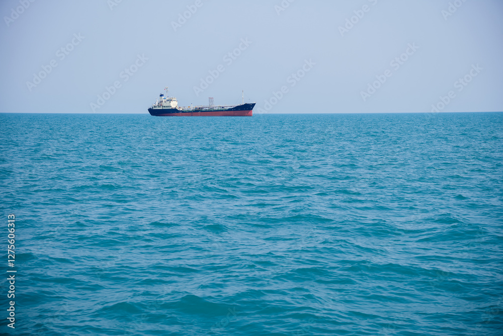 Obraz premium Cargo ship sailing across a vast, calm blue sea under a sunny sky, creating a peaceful scene of maritime transport and exploration