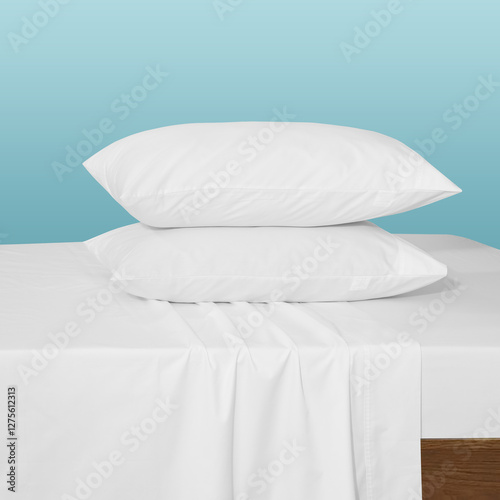 Set of white pillows on white flat sheet and fitted sheet against blue background, soft pillows on white cotton sheets against a blue background for advertising, commercial and mockup