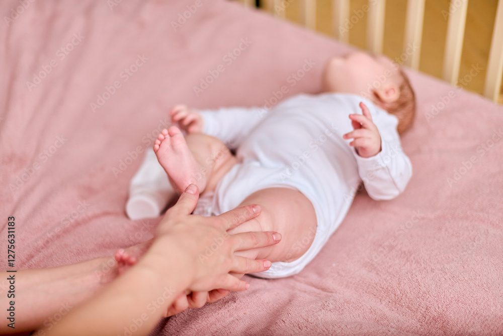 Young mother with brown hair, of caucasian descent, gently applies cream to baby girl lying on pink blanket. Bright setting emphasizes nurturing bond