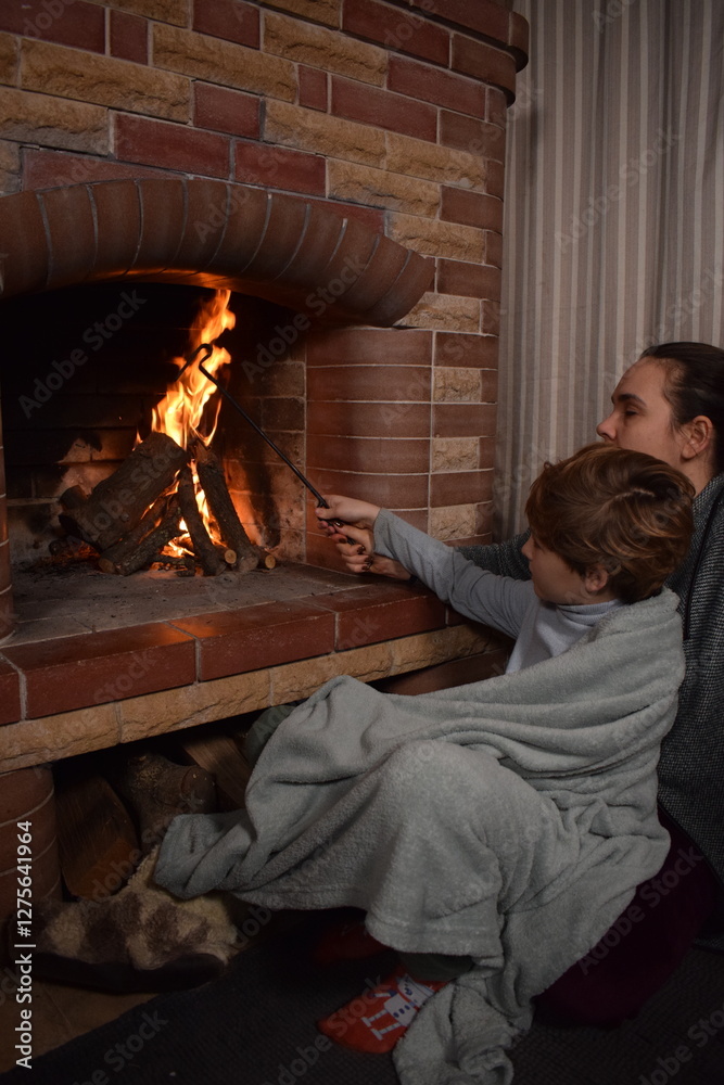 Obraz premium A young parent and child enjoy cozy leisure time by the fireplace, embracing the warmth and comfort of winter time indoors. Hygge concept. Family bonds and shares precious moments together at home