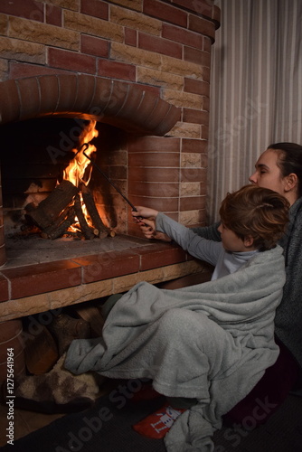 A young parent and child enjoy cozy leisure time by the fireplace, embracing the warmth and comfort of winter time indoors. Hygge concept. Family bonds and shares precious moments together at home
