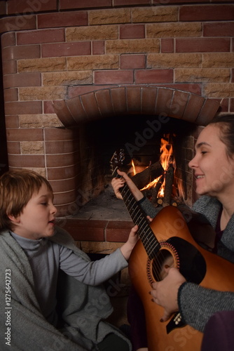 A young parent and child enjoy cozy leisure time by the fireplace, embracing the warmth and comfort of winter time indoors. Hygge concept. Family bonds and shares precious moments together at home
