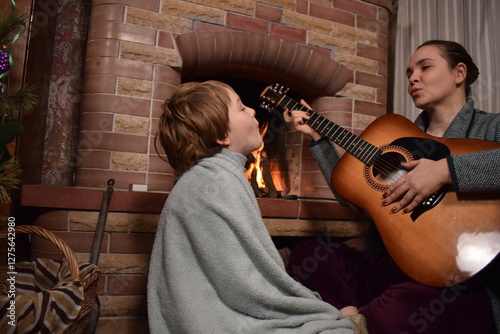 A young parent and child enjoy cozy leisure time by the fireplace, embracing the warmth and comfort of winter time indoors. Hygge concept. Family bonds and shares precious moments together at home