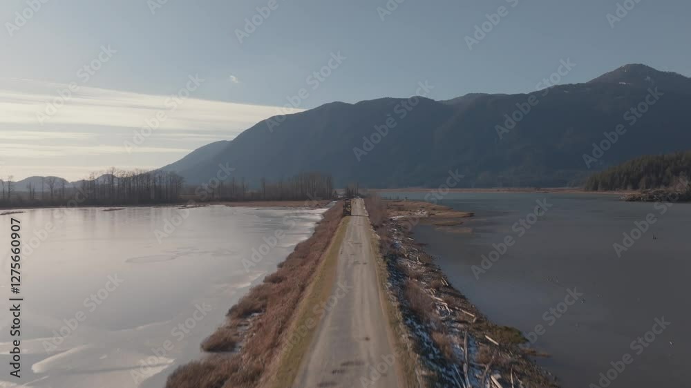 Drone view of a road extended over Pitt Lake, leading to a mountain in a sunny weather in Canada Drone view of a road extended over Pitt Lake, leading to a mountain in a sunny weather in Canada