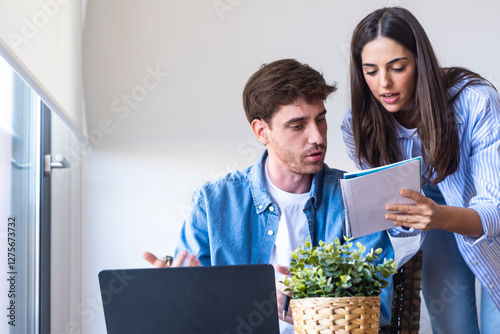 Remote workers in home office struggling with business problem, man checking financial notes while woman behind observes worried, budget issue, accounting challenge, economic stress, money decision